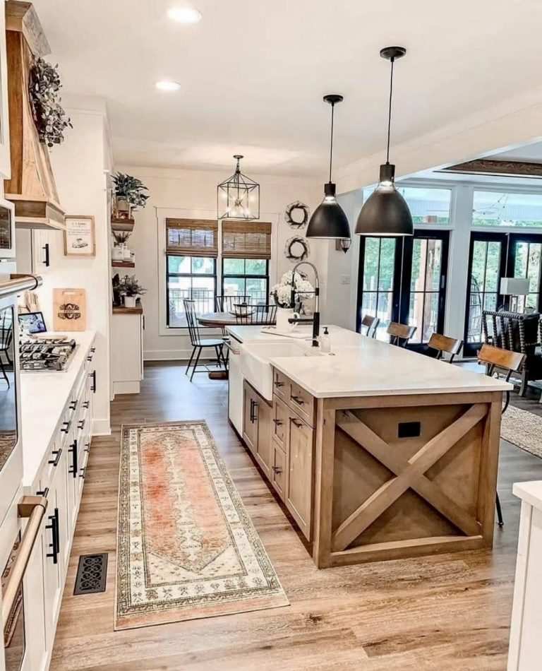Open kitchen with X‑brace wooden island, stainless steel appliances, pendant lighting, natural tones.