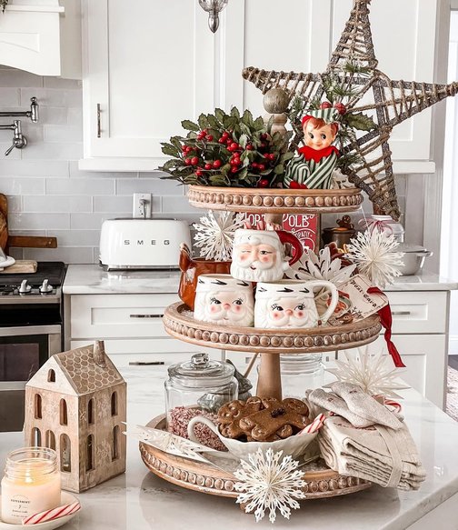 Tiered wooden tray holding Santa mugs and a mug of hot cocoa with marshmallows.