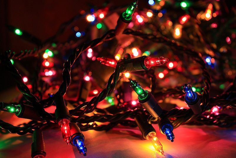 Messy tangled holiday lights laid out across a polished wooden dining table causing scratches.