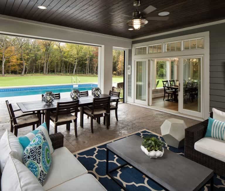 Screened in porch with a large blue area rug, white rattan furniture, and coastal decor.