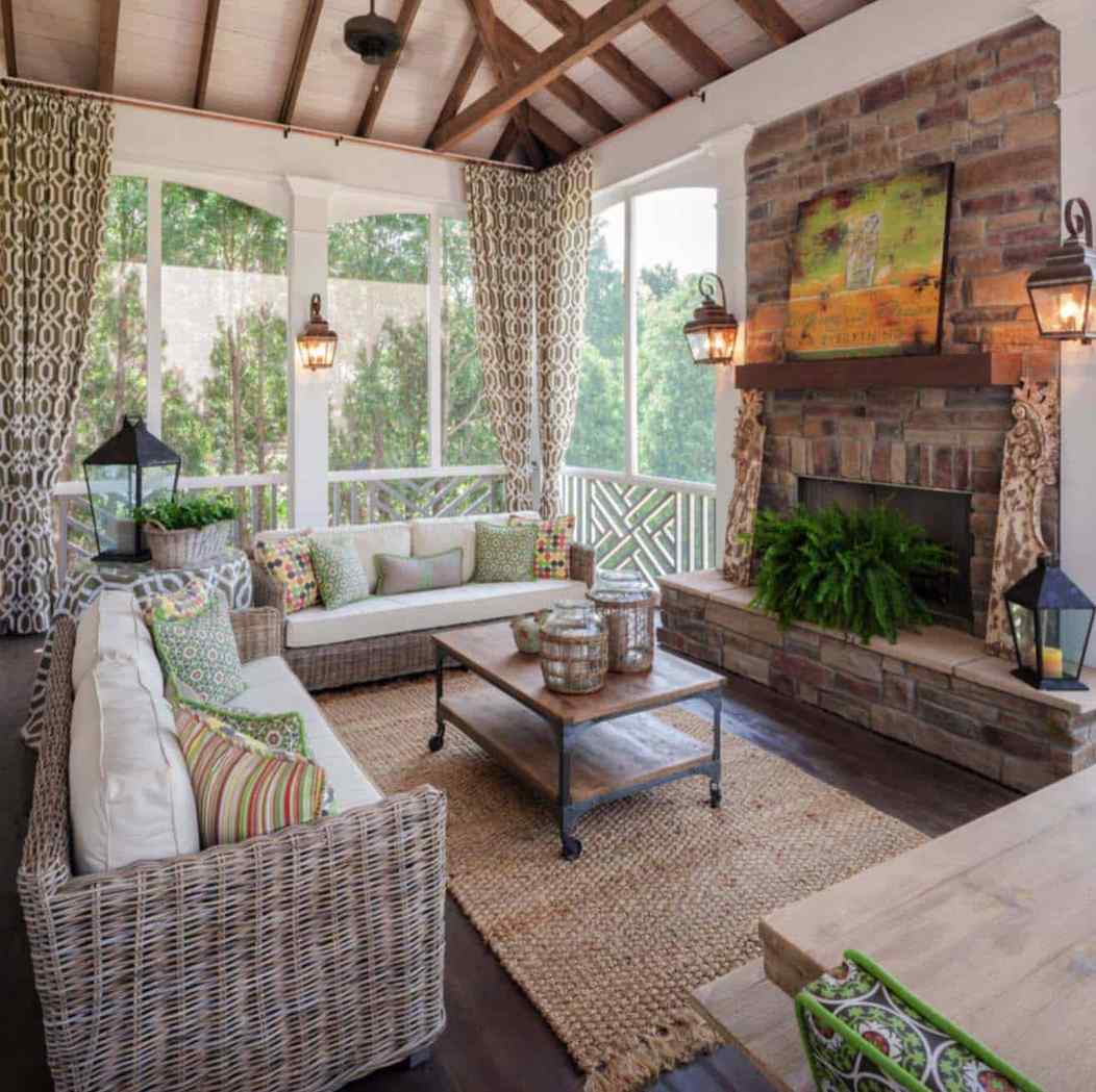 Screened in porch with brick fireplace, light flowing curtains, and wooden furniture.