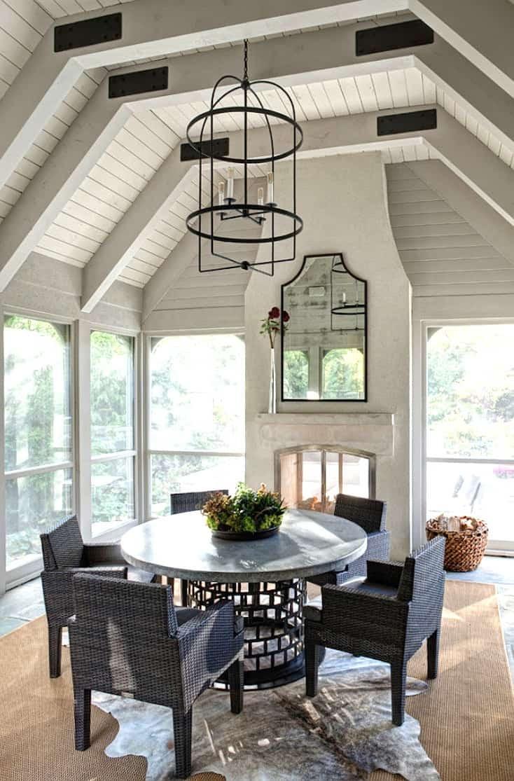 Screened in porch dining area with a stone fireplace, ornate chandelier, and large dining table.
