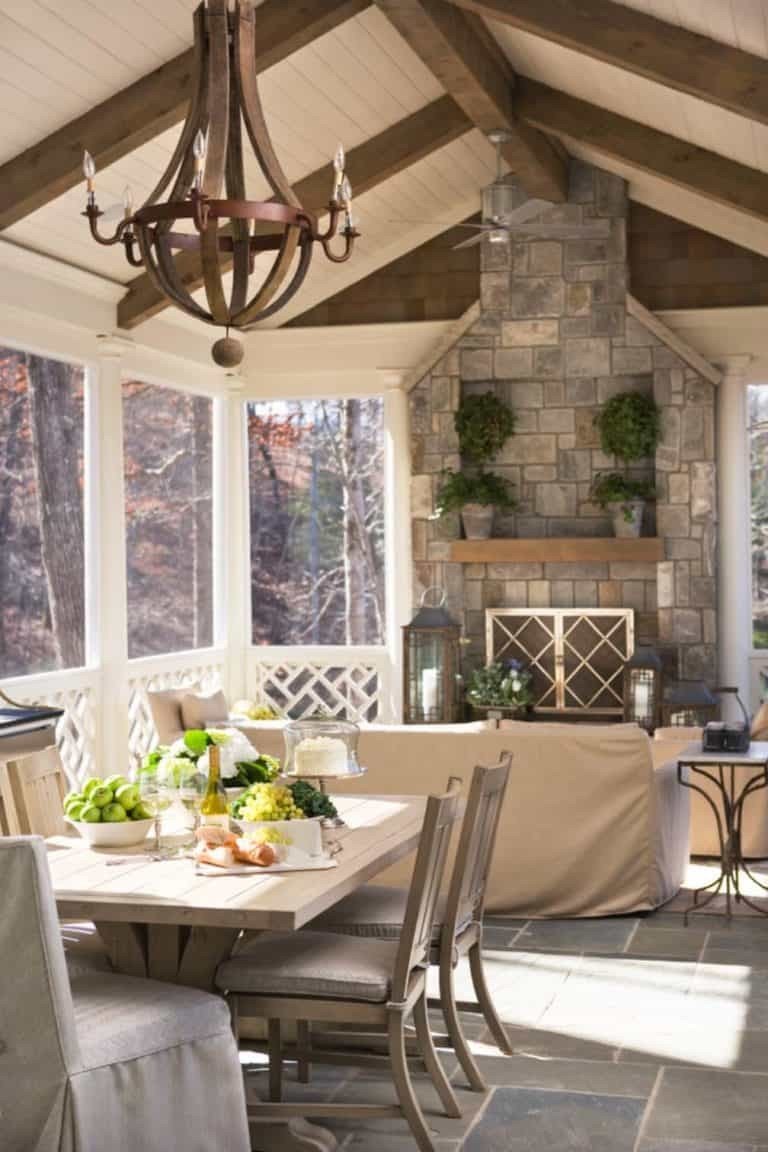 Screened in porch dining area with a massive stone fireplace, rustic table, and iron chairs.