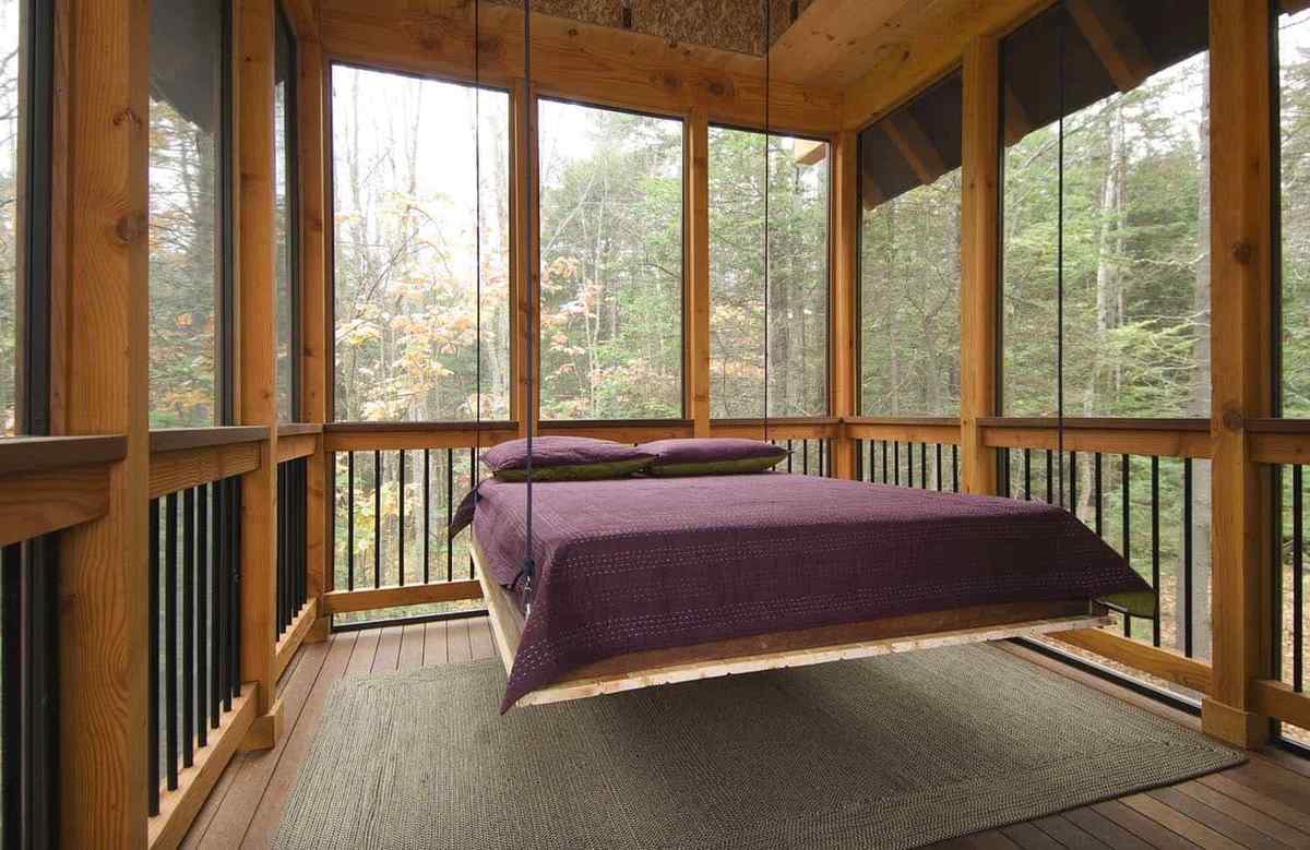 Screened in porch featuring a large hanging daybed, rope suspension, and plush pillows.