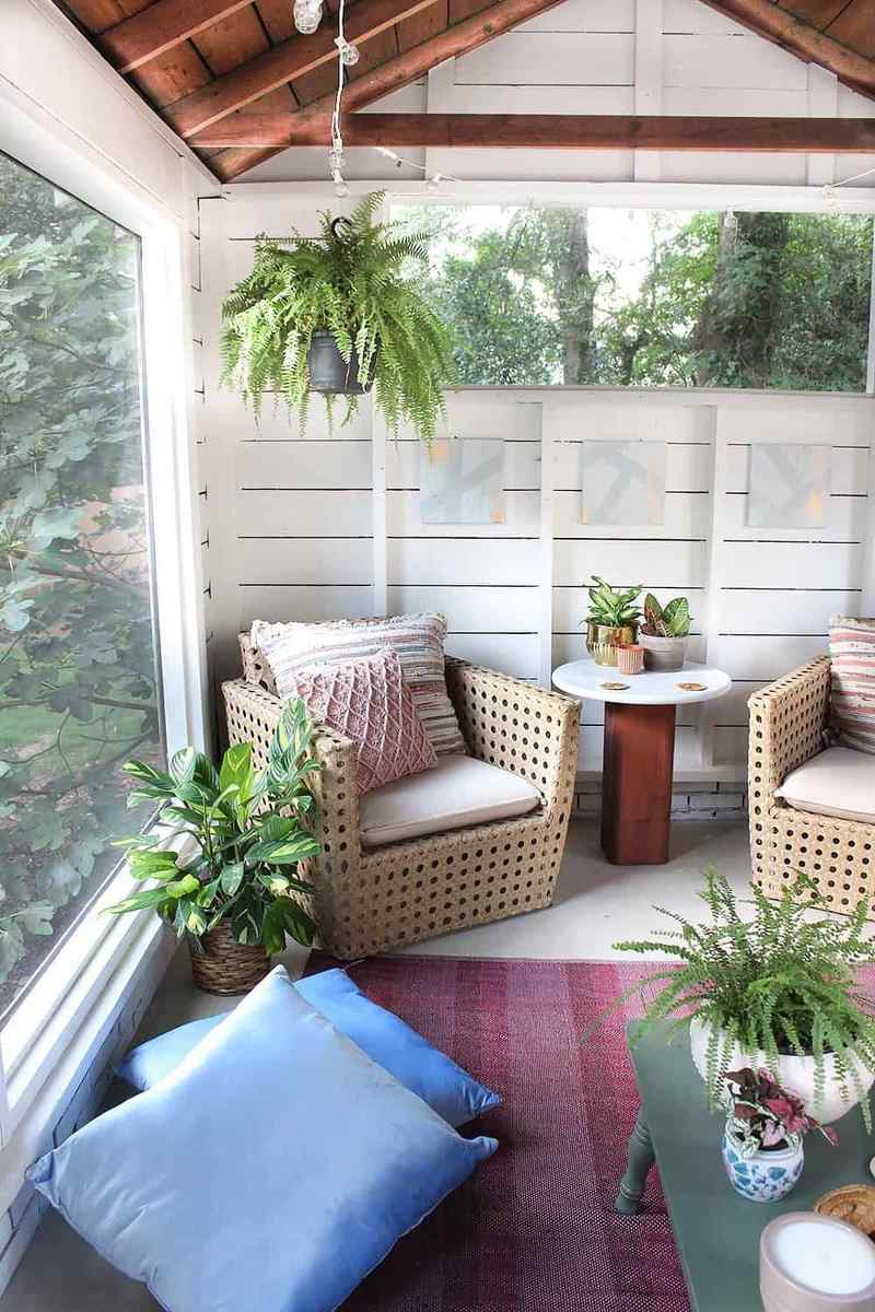Screened in porch ideas rattan chairs hanging fern featuring bohemian decor and organic textures.