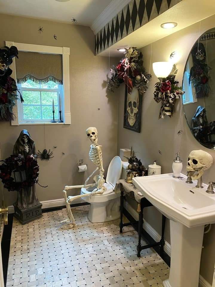 Bathroom toilet with skeleton perched, grim reaper statue, matte black tiles, cool blue lighting.