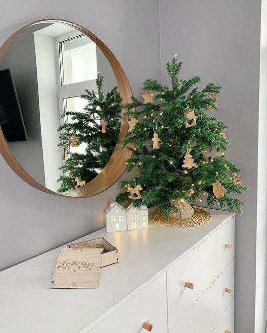 Small tabletop fir tree decorated with silver ornaments, a gold star topper, and soft white LED lights on a side table.