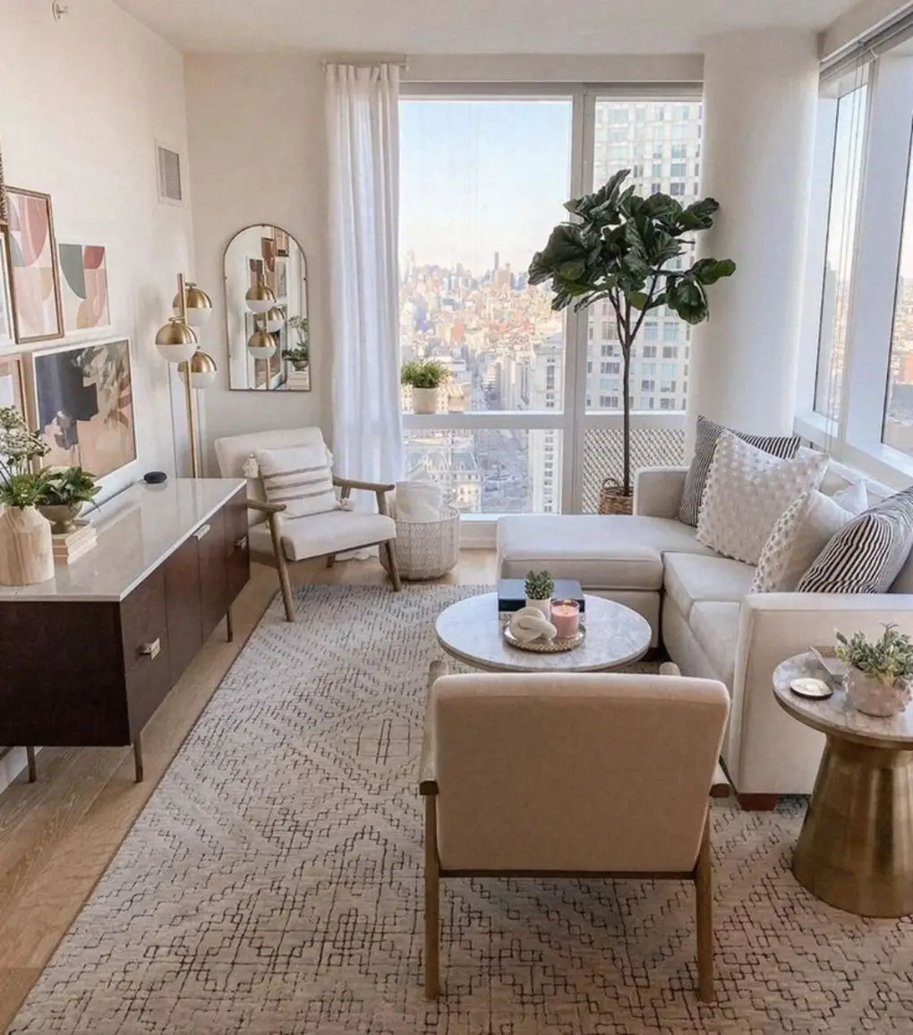 Small apartment living room with white sectional, large window with city view, and sheer white curtains.