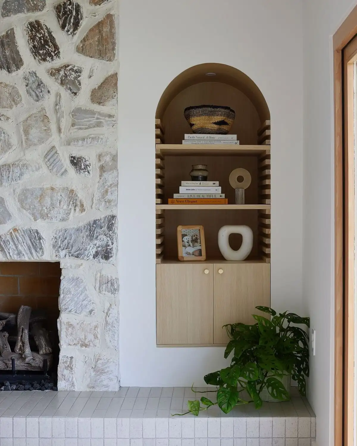 Small living room with arched wooden alcove, stone fireplace, and neutral leather armchair in soft natural light.