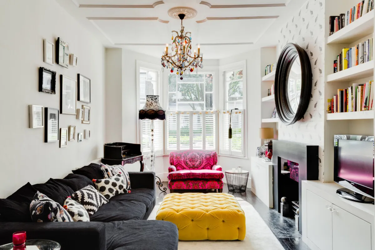 Small living room with bay window, colorful eclectic decor, and bright natural light in a vibrant setting.