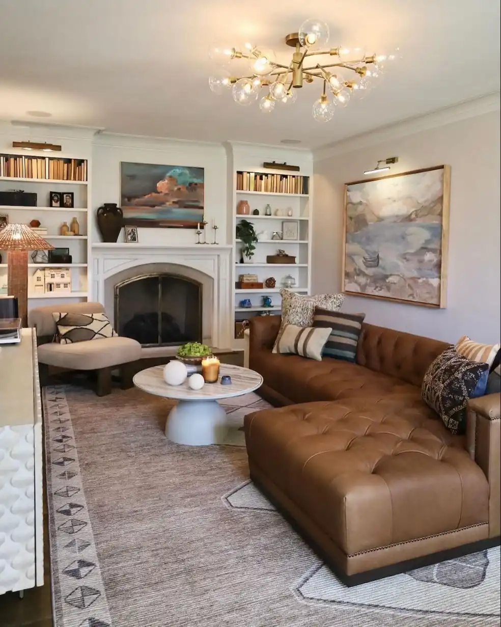 Small living room with leather sectional, brick fireplace, and built-in bookshelves in warm ambient lighting.