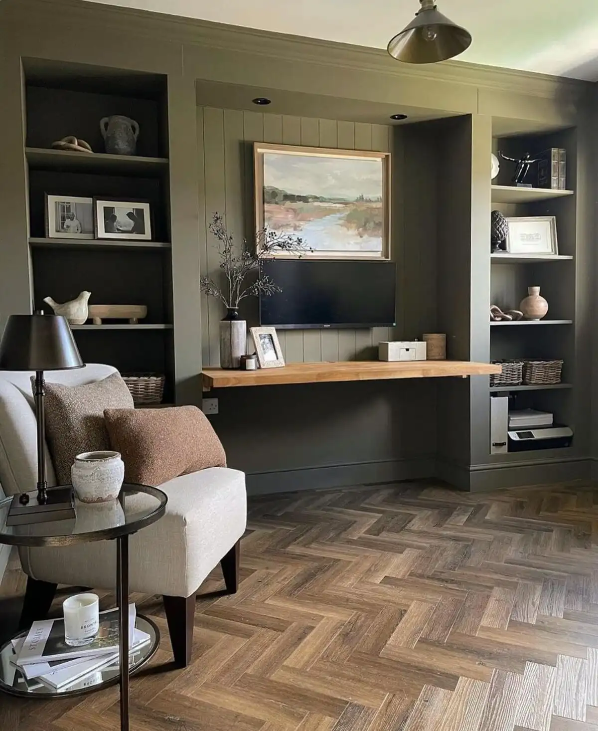 Small living room with olive green built-in TV unit, herringbone wood floor, and natural light in a stylish setting.