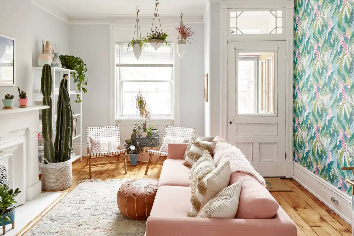 Small living room with pink sofa, botanical wallpaper, and green plants in soft natural light.