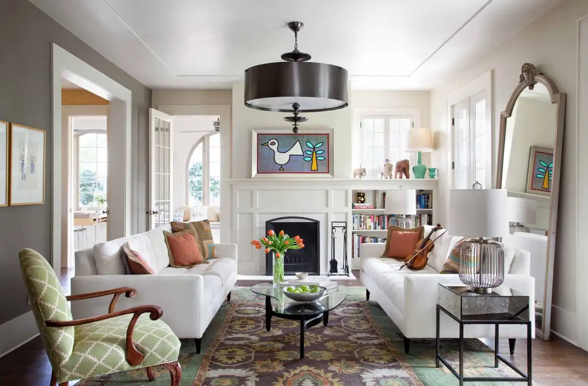 Small living room with white sofas, white fireplace, and statement chandelier in bright, elegant lighting.