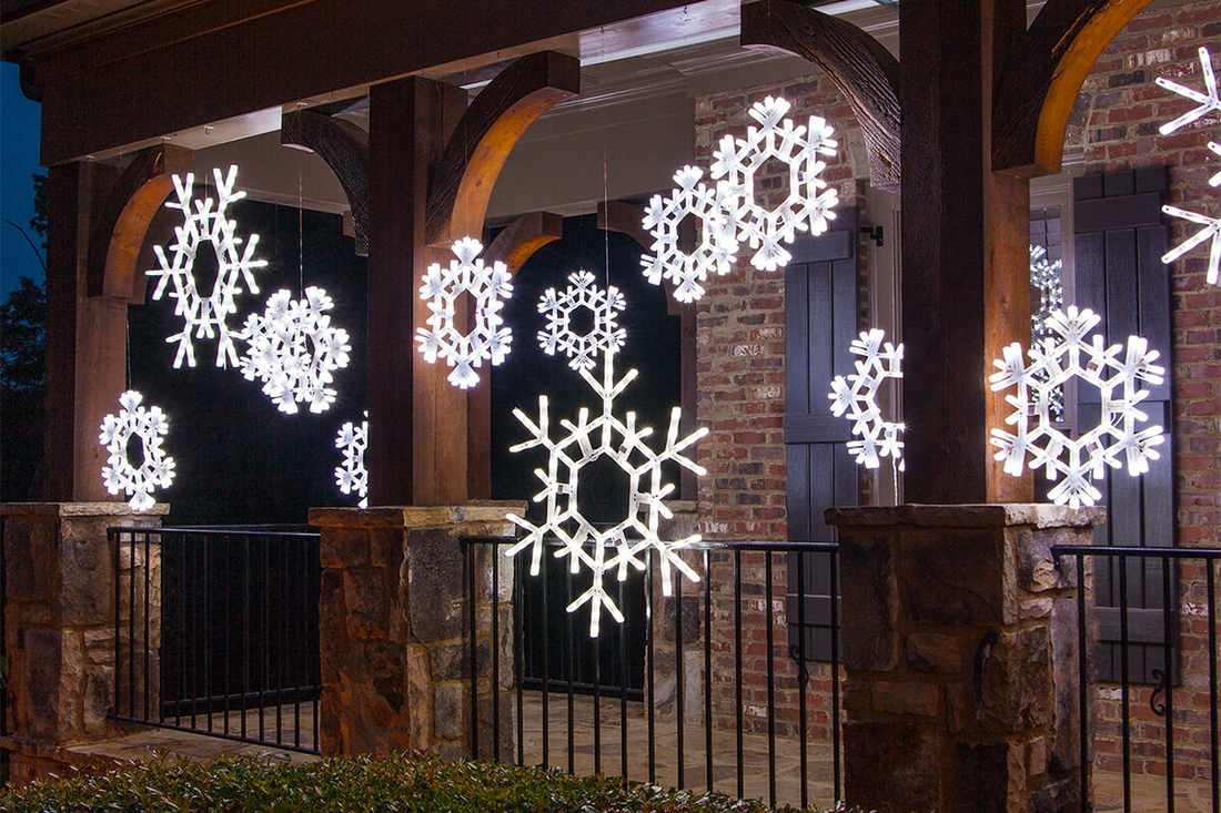 Delicate snowflake-shaped light displays hanging from a porch ceiling as outdoor christmas decorations.