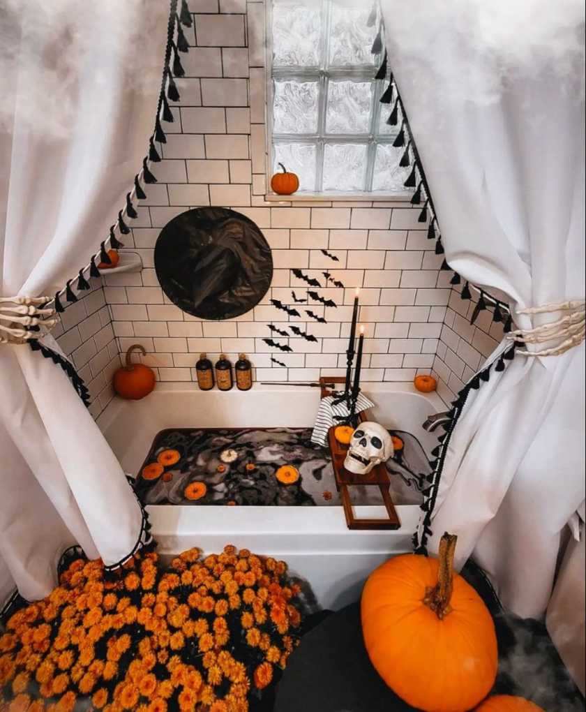 Freestanding bathtub, skeleton hand curtain tie‑backs, marigold floral accents, dark stone tiles, warm candlelight.
