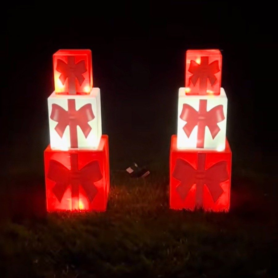 A stack of glowing, decorative gift boxes placed near a doorway as outdoor christmas decorations.