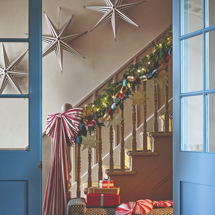 Grand foyer curved staircase banister wrapped in lush evergreen garland with warm fairy lights and ribbon