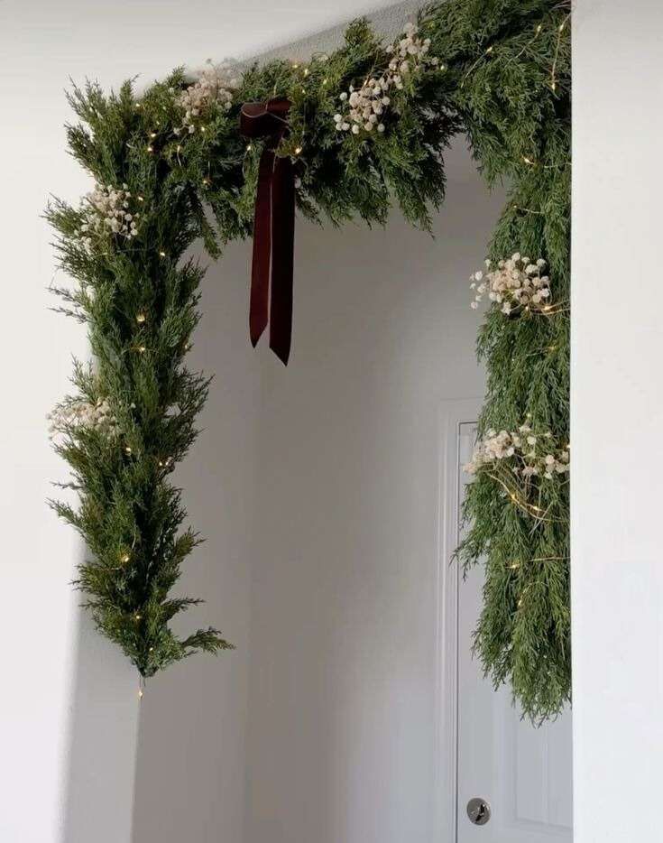 Staircase railing wrapped in a lush evergreen garland, topped with a small pine wreath and tiny white lights.