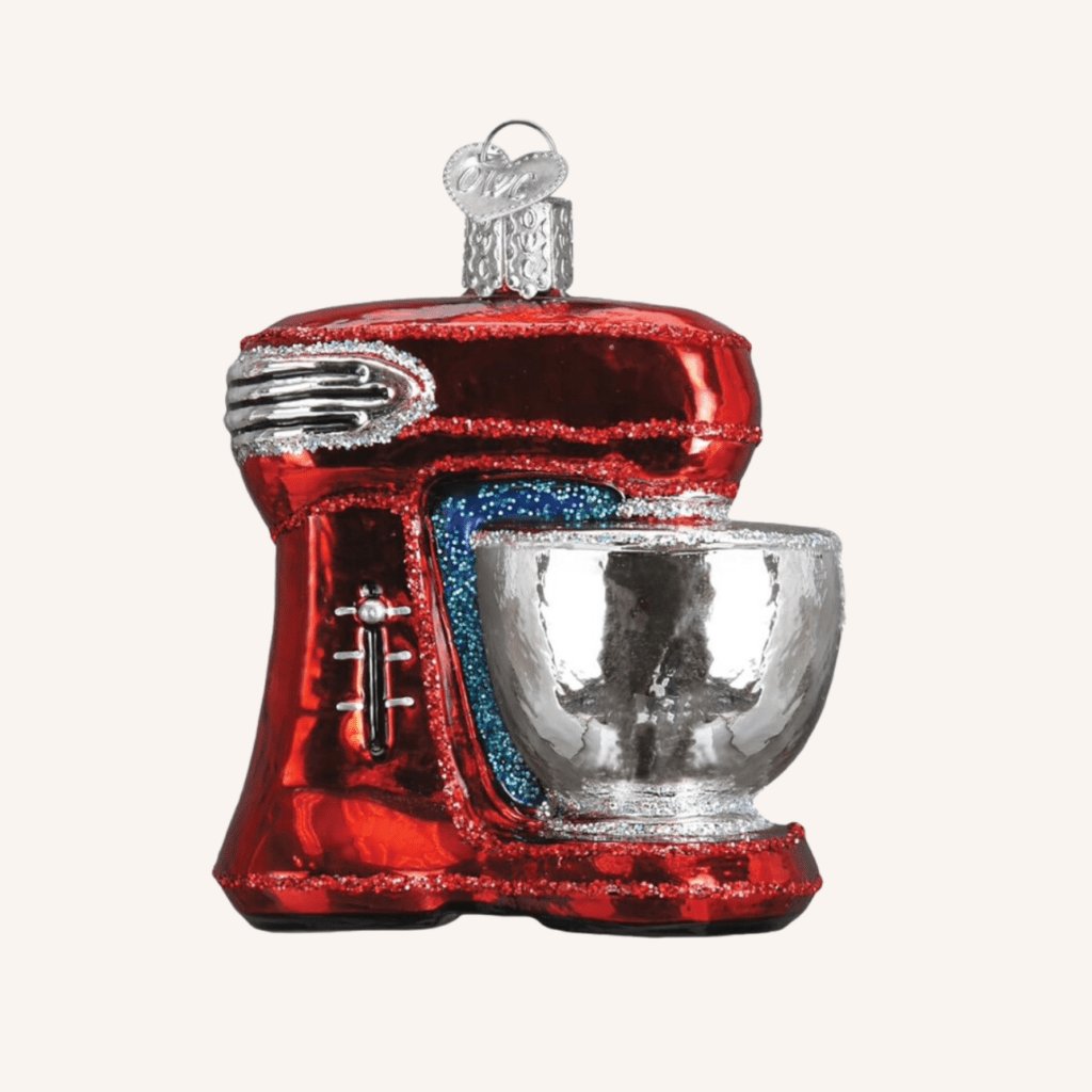 Small red stand mixer ornament hanging on a tree branch with other kitchen-themed decorations.