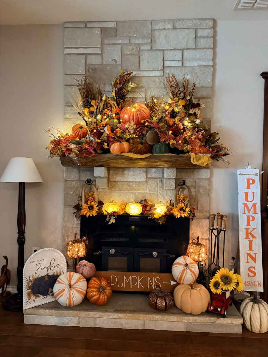 Stone fireplace wall, rustic stone mantel, cluster of orange pumpkins, woven basket, soft candlelight.