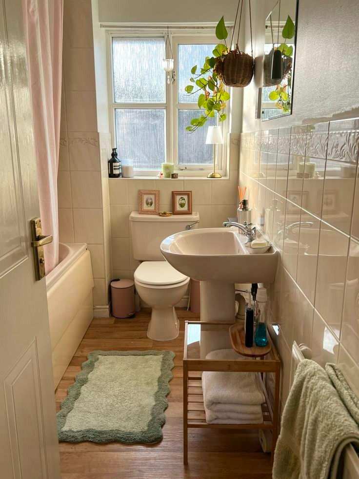 Bright cottage bathroom showcasing white shiplap walls, hanging potted plants, a vintage clawfoot tub, and natural light.