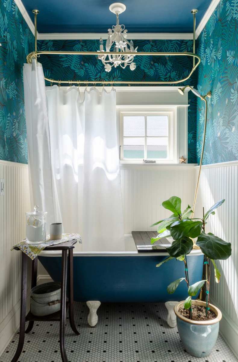 Vibrant teal blue bathroom walls housing a restored white clawfoot tub with ornate silver feet.