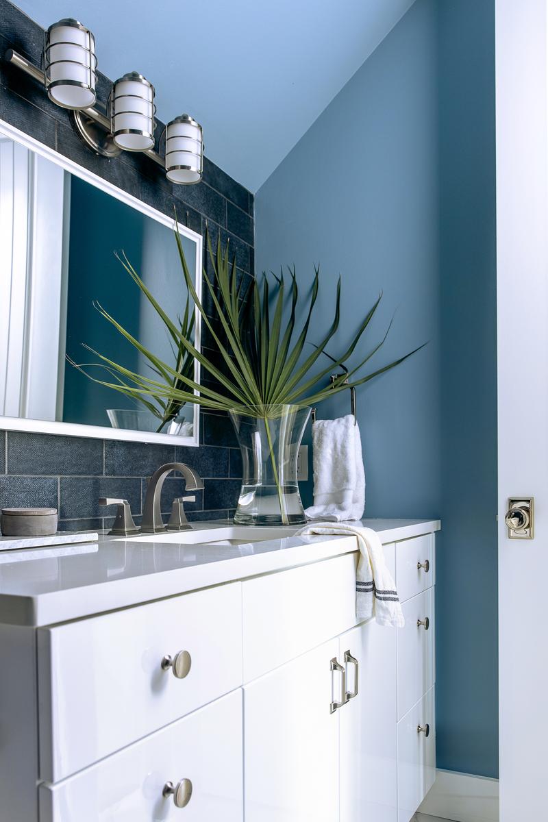 Crisp white bathroom vanity against rich saturated teal blue walls and polished chrome hardware.