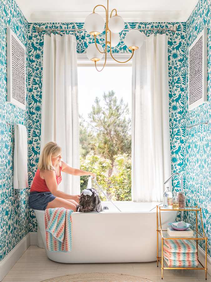 Freestanding white soaking tub set against lush teal botanical wallpaper and matte black hardware.