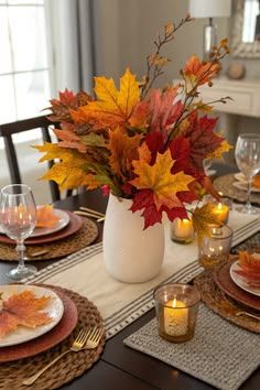 Dining table with large clear vase, autumn leaves, multiple candles, soft ambient lighting