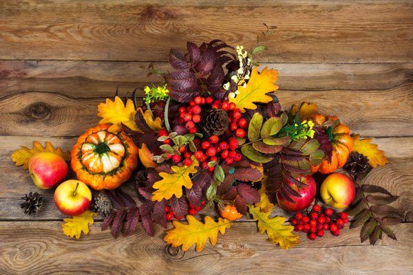 Traditional woven seagrass cornucopia overflowing with apples pomegranates and autumn leaves on rustic wood