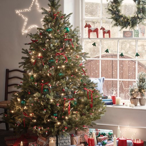 Cozy den featuring traditional red green ribbon tree by brick fireplace in warm lamplight