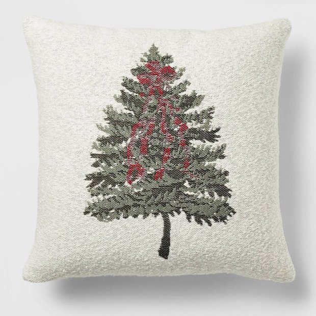 Cream linen throw pillow with a red embroidered christmas tree design on a wooden armchair.