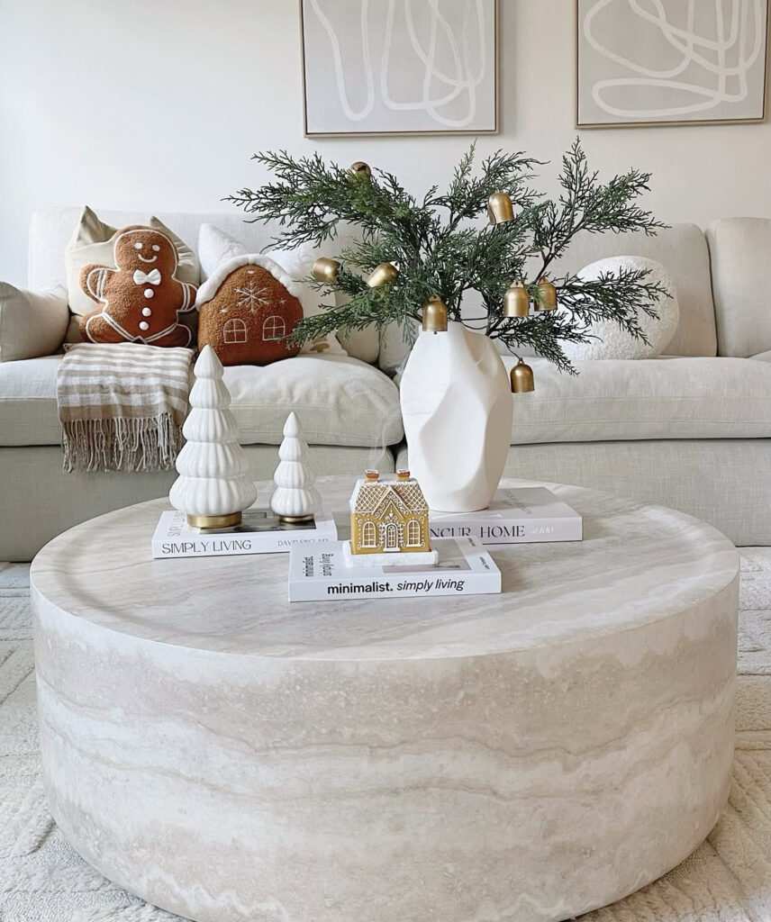 Christmas coffee table decor featuring a tall glass vase of pine greenery adorned with brass bells.
