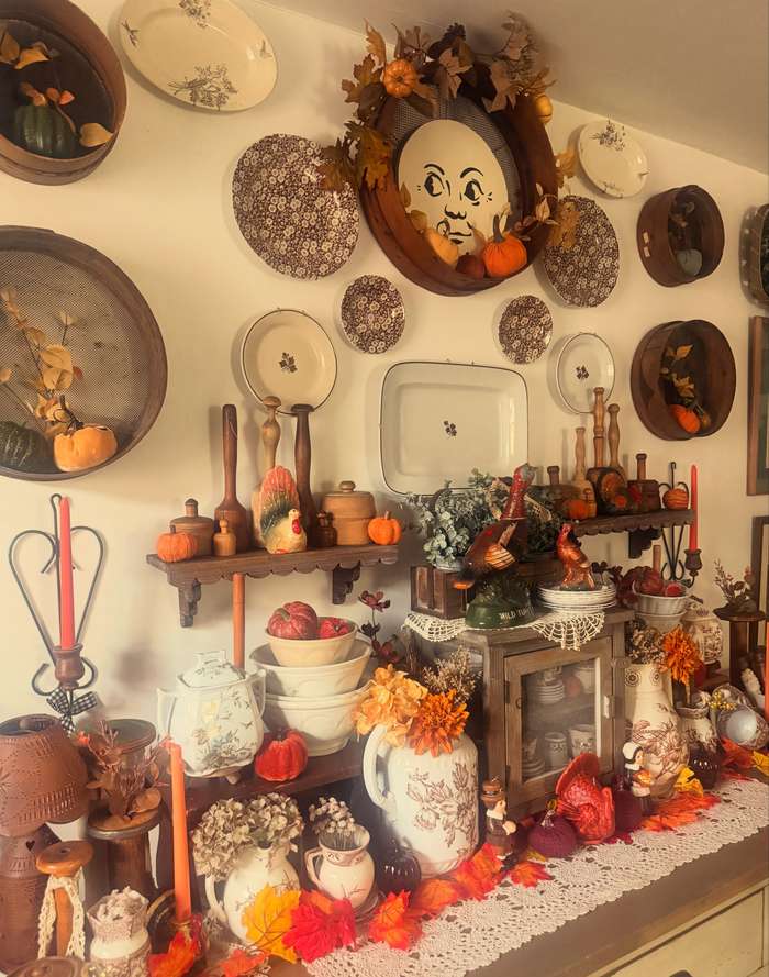 Kitchen dining wall, assorted vintage plates, mini pumpkin ornaments, brushed brass hooks, soft pendant lighting.