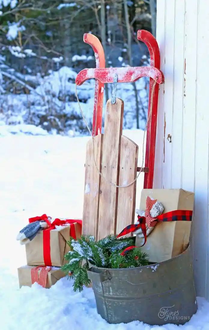 A vintage wooden sled leaned against a porch wall with greenery as outdoor christmas decorations.