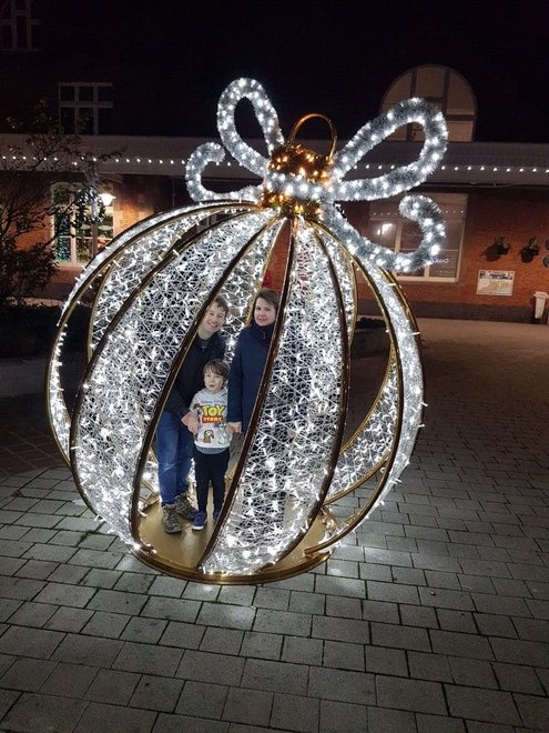Large walk in giant Christmas ornament sculpture made of gold metal and sparkling lights on driveway pavers.