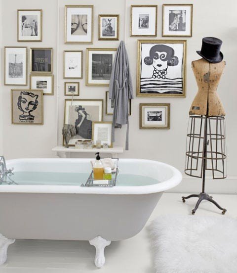 White bathroom design ideas showcasing clawfoot tub, botanical gallery wall, brass frames, and warm light