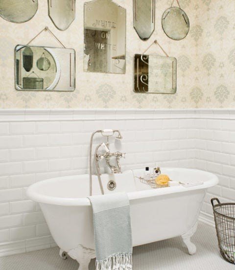 Elegant white bathroom with clawfoot tub, antiqued mirrored wall panels, polished chrome, and soft sconces