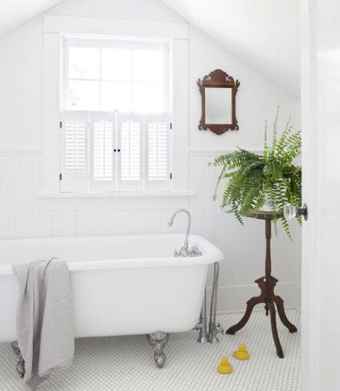 Crisp white bathroom with clawfoot tub, wide louver plantation shutters, soft morning light, and linen textiles