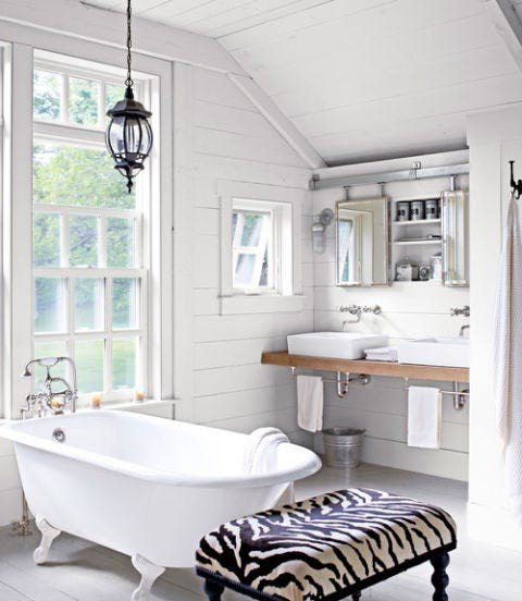 Contemporary white bathroom with freestanding clawfoot tub, zebra print vanity stool, brass hardware, and neutral tiles