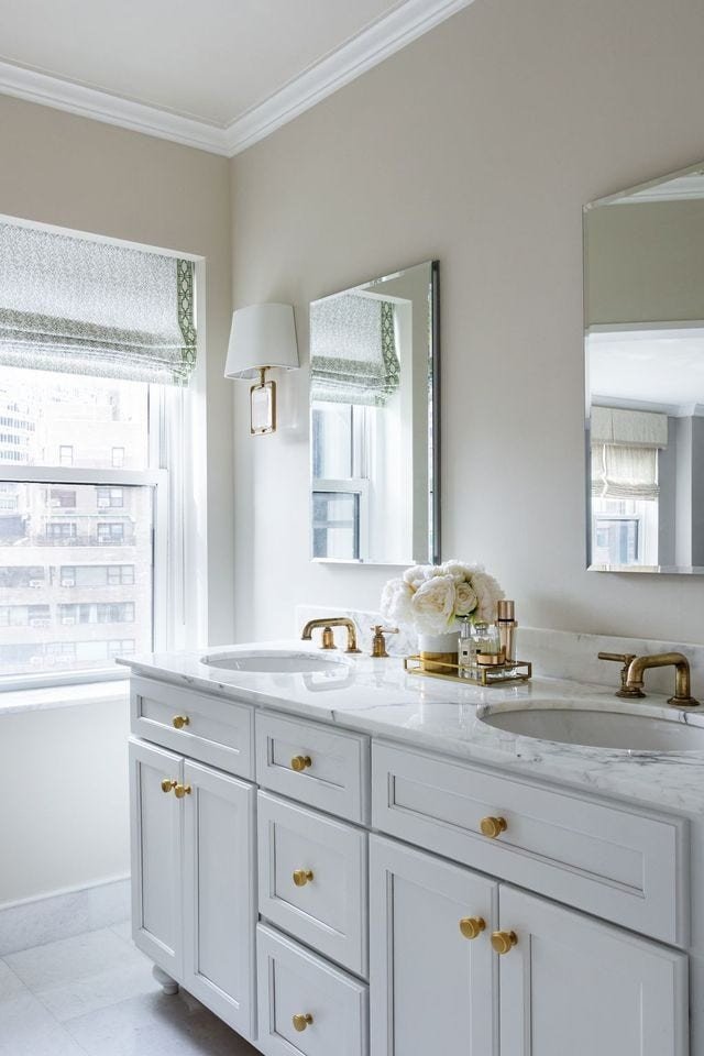 White bathroom design ideas featuring white double vanity, unlacquered brass hardware, twin mirrors, and marble counters