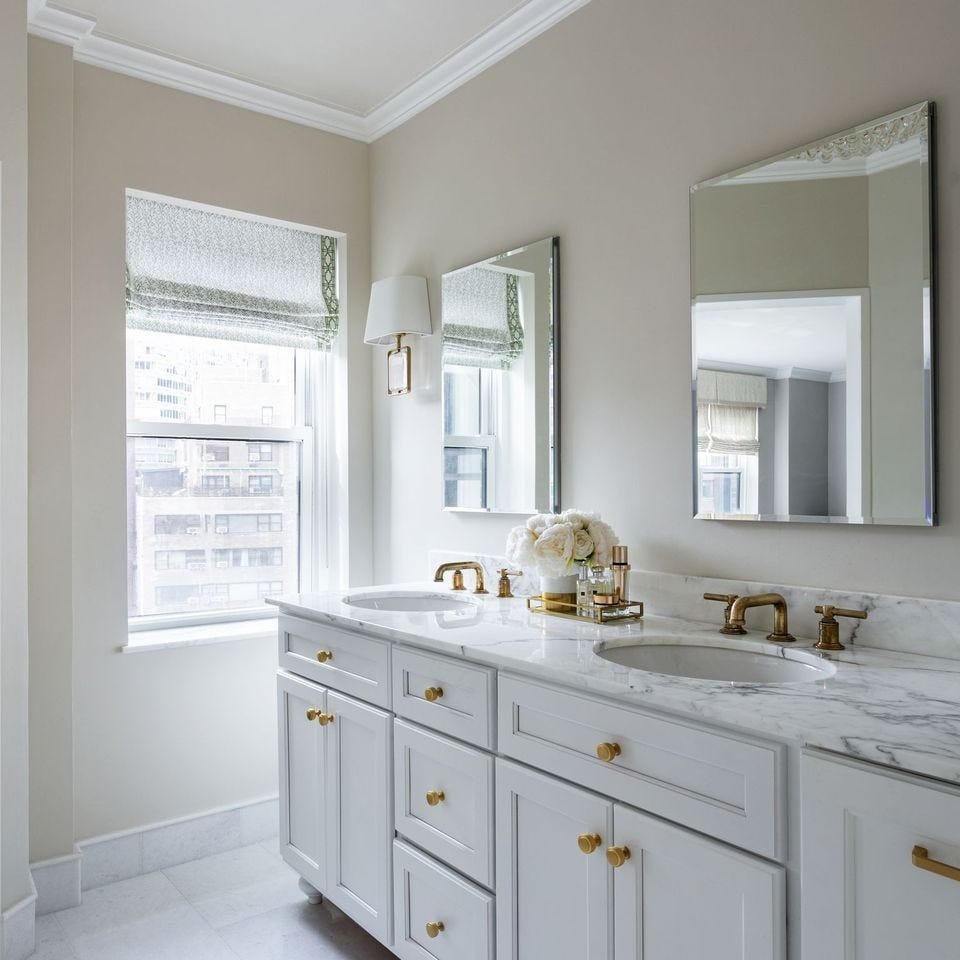 Luxury white bathroom featuring statuary marble double vanity, integrated sinks, white walls, and backlit mirrors