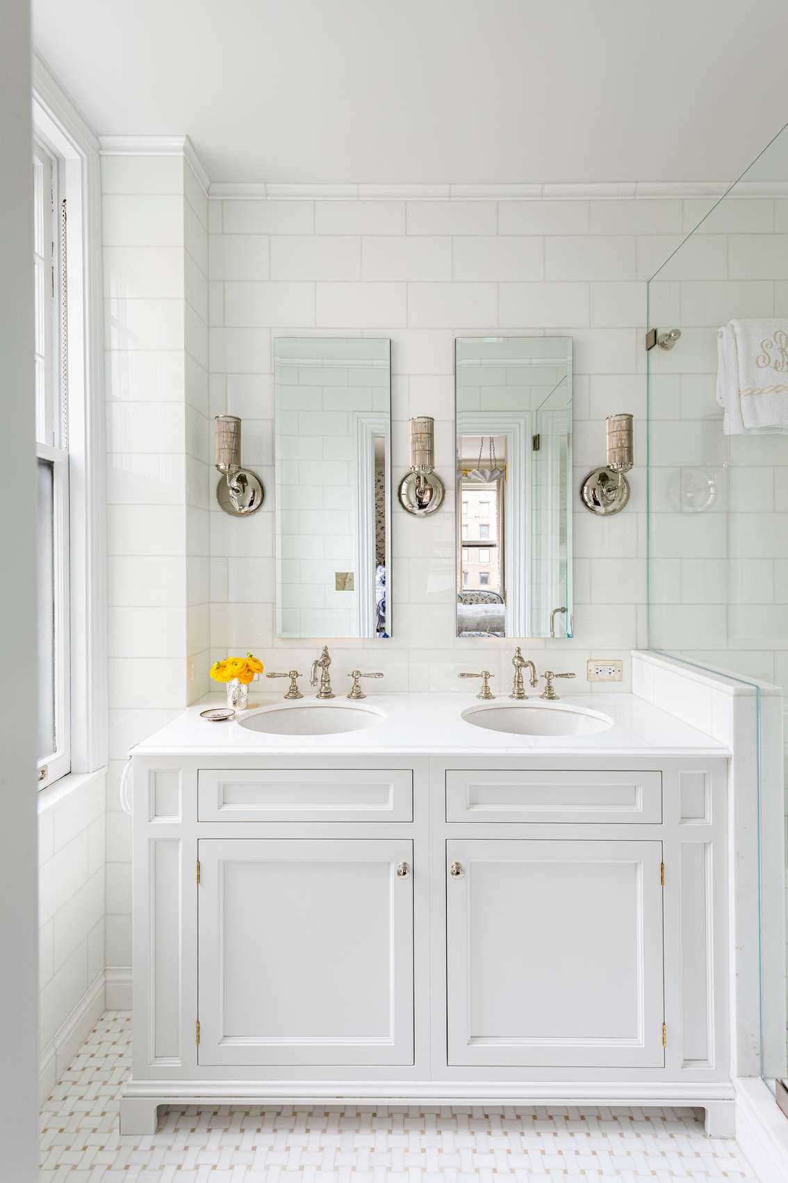 Minimalist white bathroom featuring handleless double vanity, white solid surface counters, and frameless mirrors