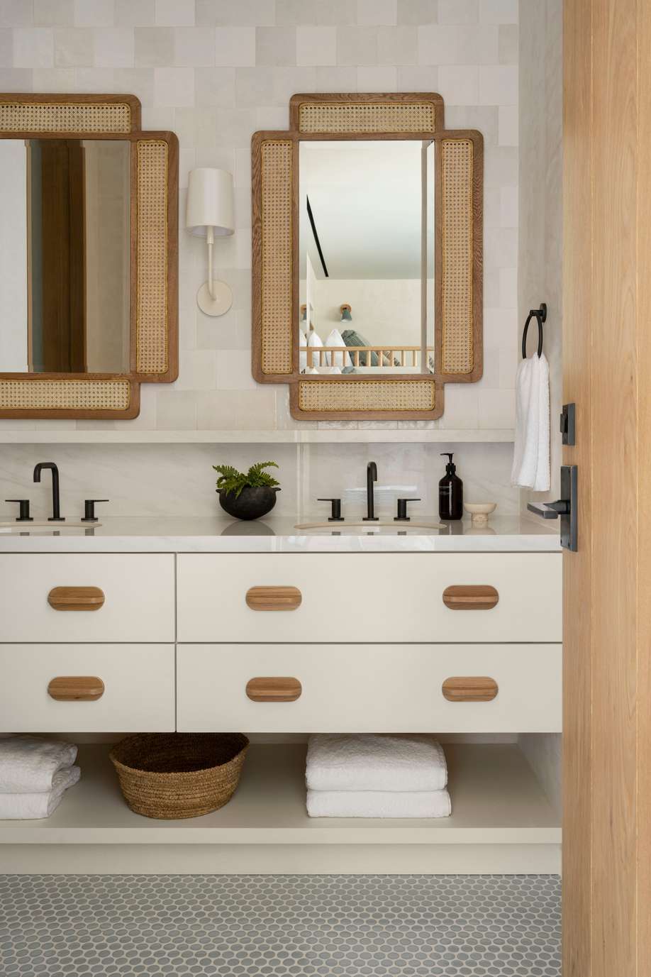 Bright white bathroom design featuring white double vanity, woven rattan mirrors, brass faucets, and natural textures