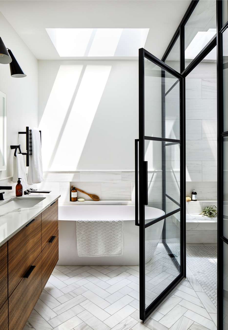 White bathroom design ideas featuring herringbone tile shower, clear glass enclosure, matte black trim, and bright light