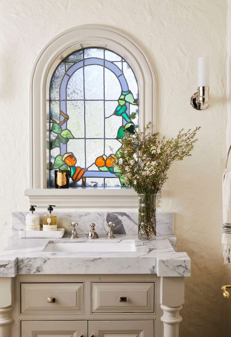 White bathroom design ideas showcasing marble vanity, historic stained glass window, warm lighting, and white walls