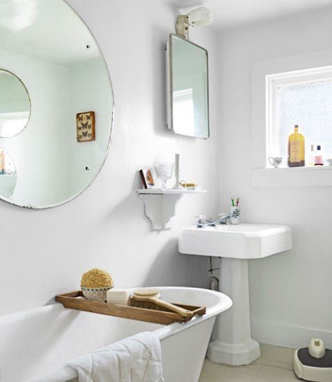 Modern white bathroom design ideas highlighting a sleek round mirror mounted above a porcelain pedestal sink.