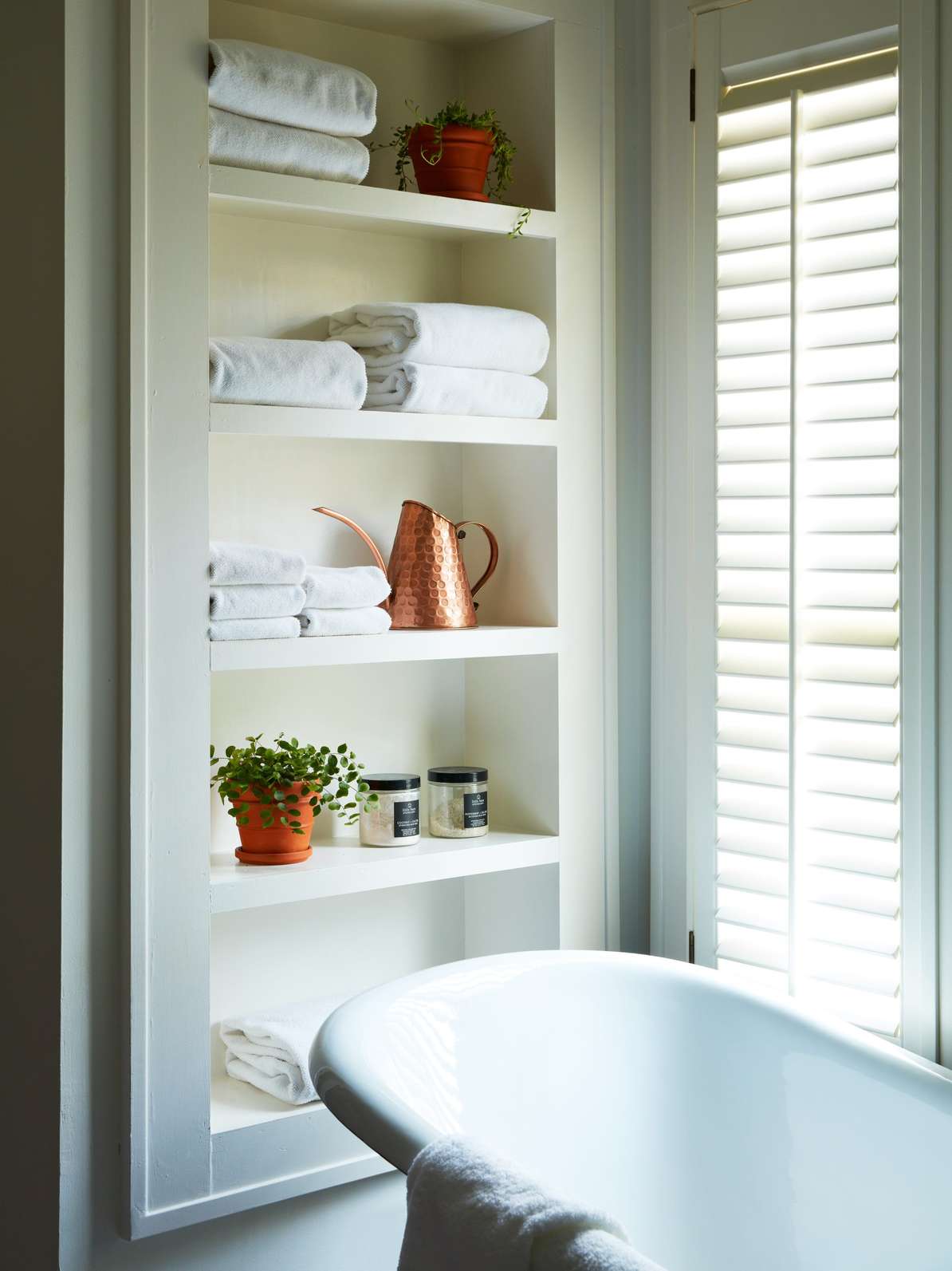 Smart white bathroom design ideas displaying open built-in towel shelves directly above a contemporary freestanding bathtub.