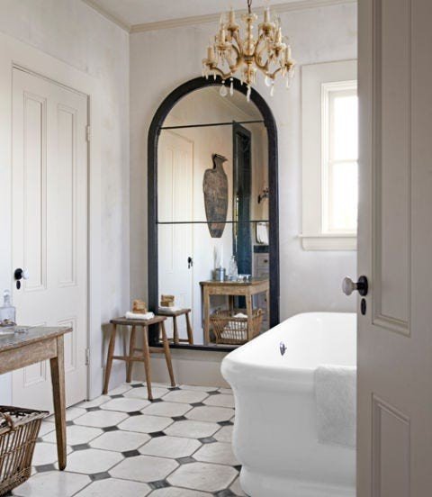 Modern white bathroom design ideas displaying a freestanding tub placed beneath a dramatic brass arched wall mirror.